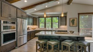 A modern kitchen with built-in appliances, a large island with stools, and a view of the outdoors. - In the Wild Woods - TLUXP (Tahoe Vista)