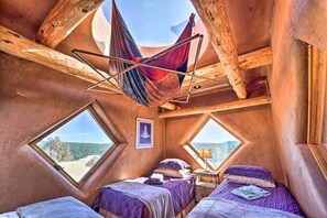 Un cuarto acogedor de techo triangular con dos camas, una hamaca y grandes ventanales que ofrecen vistas panorámicas.