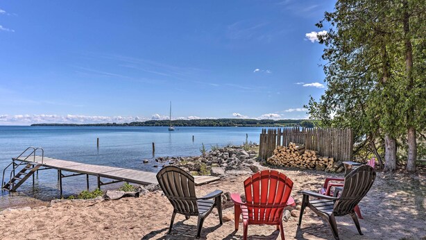Un espacio de descanso frente a la playa con dos sillas Adirondack, un muelle de madera y vistas al lago.