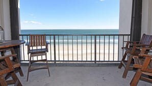 Un balcon avec vue sur la plage, des chaises en bois et une table.