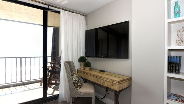 Un balcon avec une chaise et une table, un bureau avec une télévision et une bibliothèque remplie de livres et d’objets décoratifs.