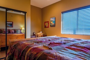 A bedroom with a bed, a dresser, a chair, a window with blinds, and a painting on the wall.