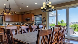 A spacious dining area with a large table and chairs, a kitchen with wooden cabinets, and a view of the outdoors through large sliding glass doors.