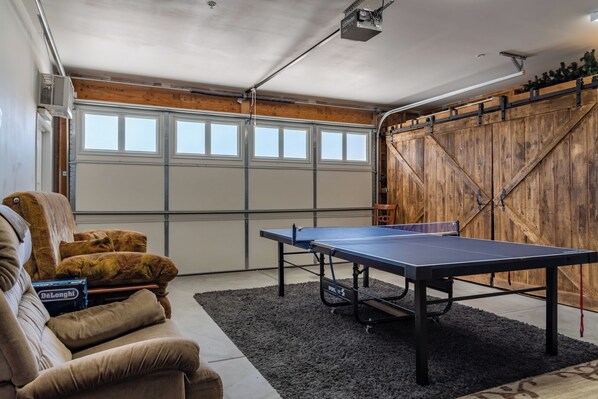 A room with a ping pong table, a couch, and a wooden wall.