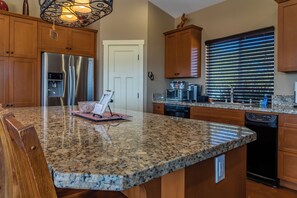 A kitchen with granite countertops, wooden cabinets, a stainless steel refrigerator, a coffee maker, and a window with blinds.