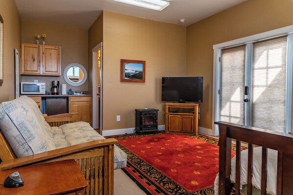 A living room with a sofa, a television, a fireplace, and a kitchen area with cabinets and a microwave.