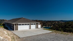 Ein eingeschossiges Gebäude mit Garage, einer überdachten Veranda und Blick auf einen See und Hügel im Hintergrund.