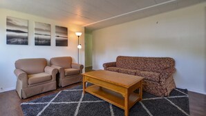 Ein Wohnzimmer mit zwei Sesseln, einem Sofa, einem Couchtisch aus Holz und einem gemusterten Teppich.