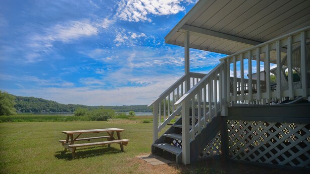 Eine Holzterrasse mit Picknicktisch, einer Treppe und Blick auf einen See und Wald.