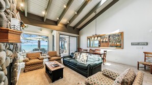 A spacious living room with a large window overlooking a scenic view, a fireplace, and a cozy seating area. - Lakefront Beauty + On Water, Lakeland Village #610 (South Lake Tahoe)