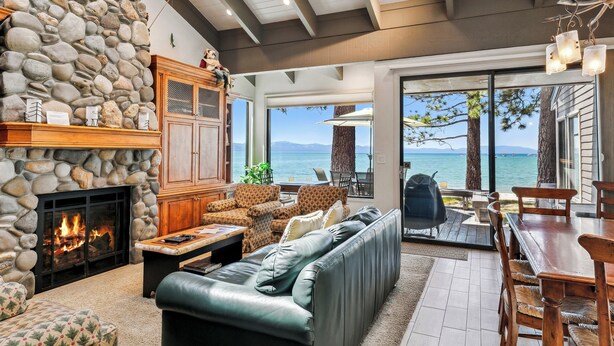 A stone fireplace, leather sofa, dining table, and outdoor seating by a scenic lake view. - Lakefront Beauty + On Water, Lakeland Village #610 (South Lake Tahoe)