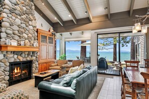 A stone fireplace, leather sofa, dining table, and outdoor seating by a scenic lake view. - Lakefront Beauty + On Water, Lakeland Village #610 (South Lake Tahoe)