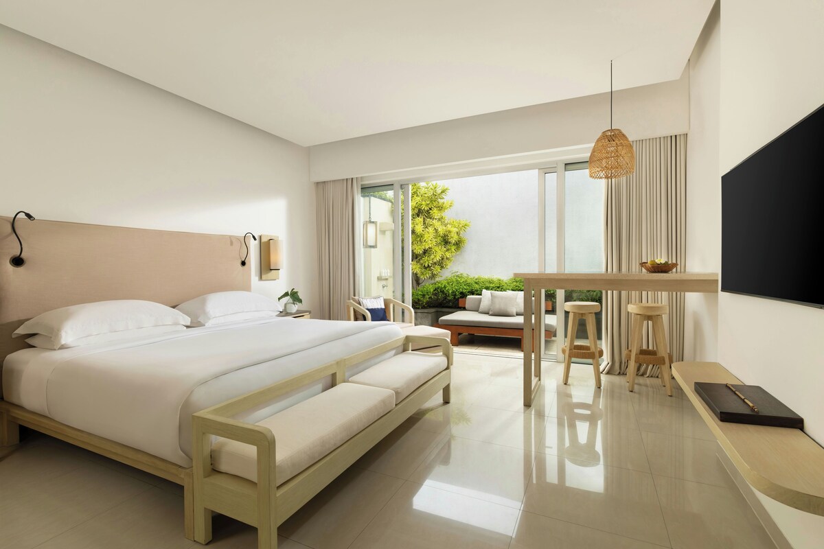 A modern bedroom with a large bed, a small table with stools, and a TV mounted on the wall.