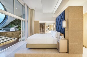A modern hotel room with a large bed, a view of the outdoors, and a stone wall.