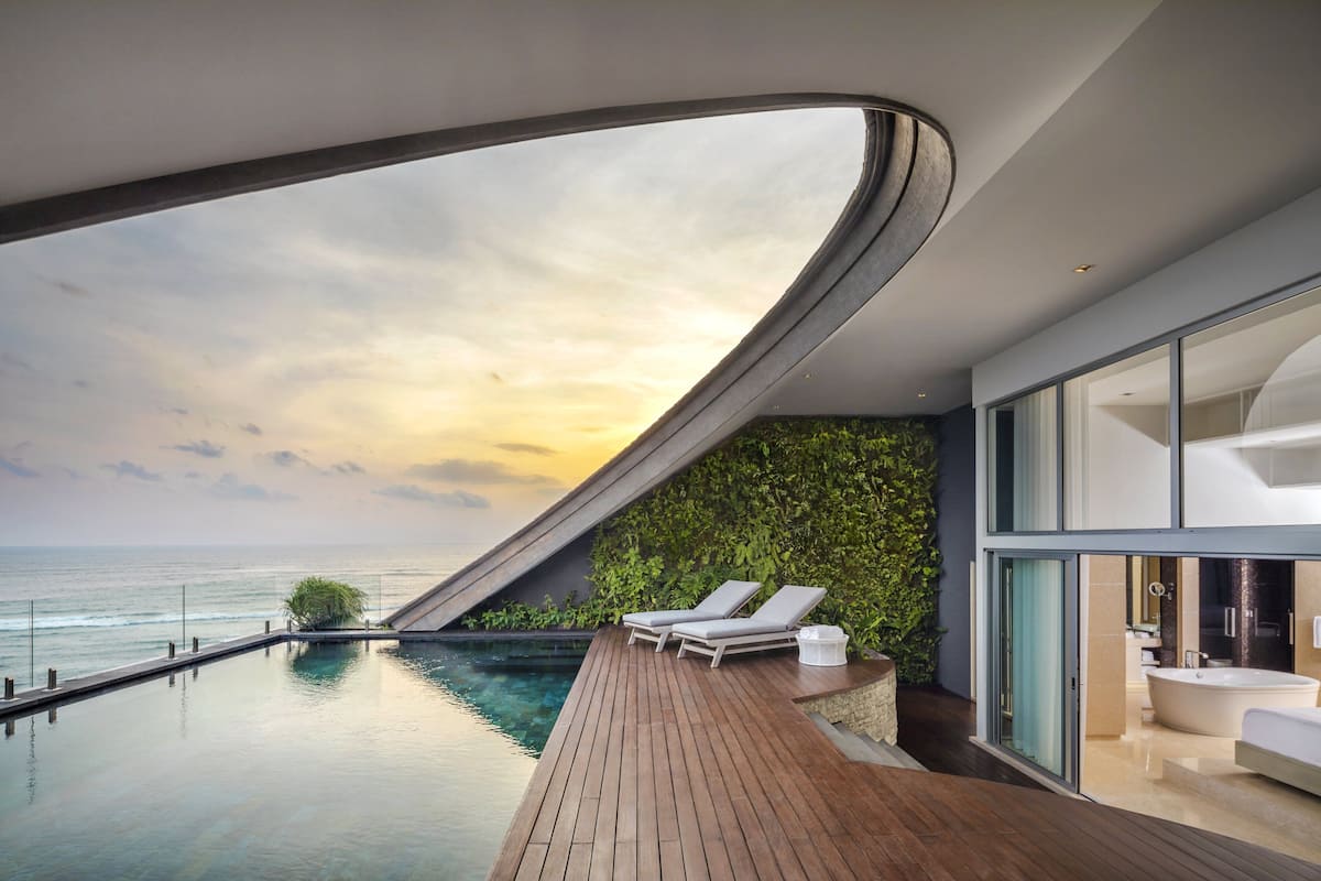 A modern infinity pool with a curved ceiling, a wooden deck, and a view of the ocean.