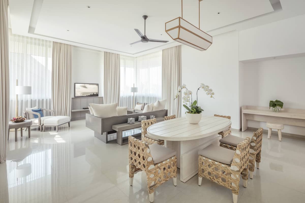 Una sala de estar moderna con un sofá blanco, una mesa de comedor con sillas de mimbre y un ventilador de techo.