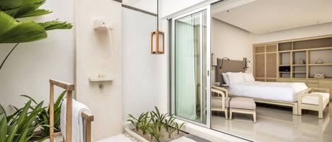 A modern hotel room with a large bed, a glass door leading to a balcony, and a small seating area.