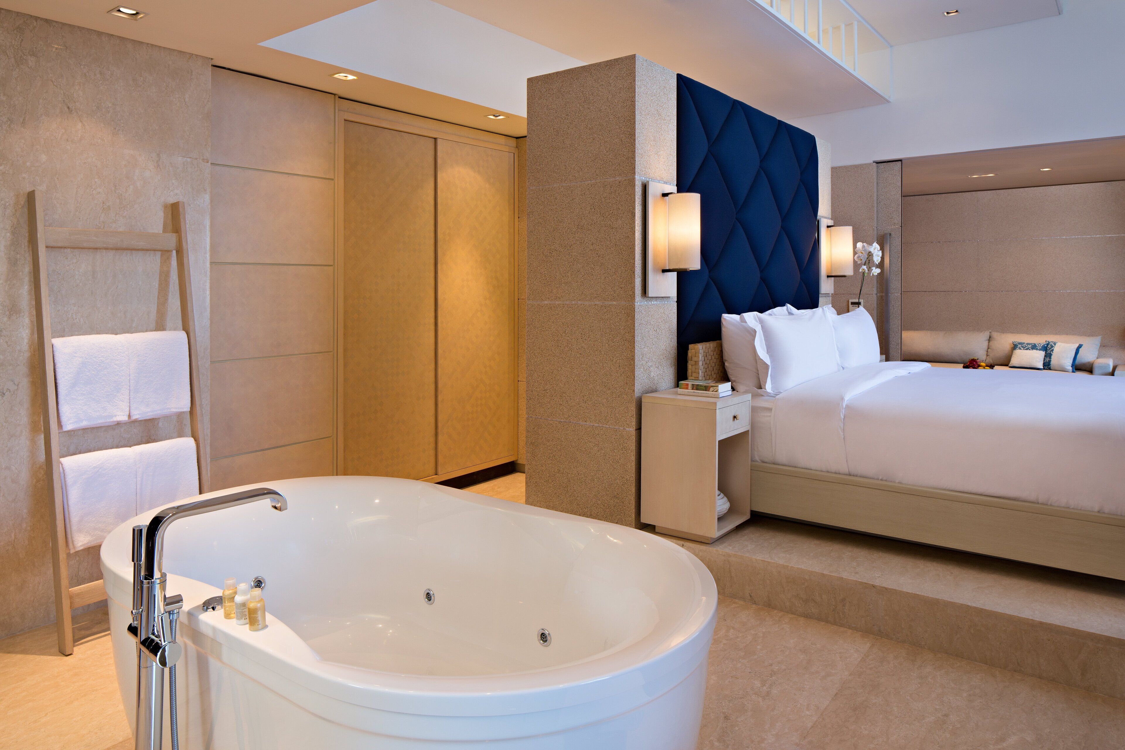 A modern hotel room with a large bathtub, a neatly made bed, and a built-in wardrobe.