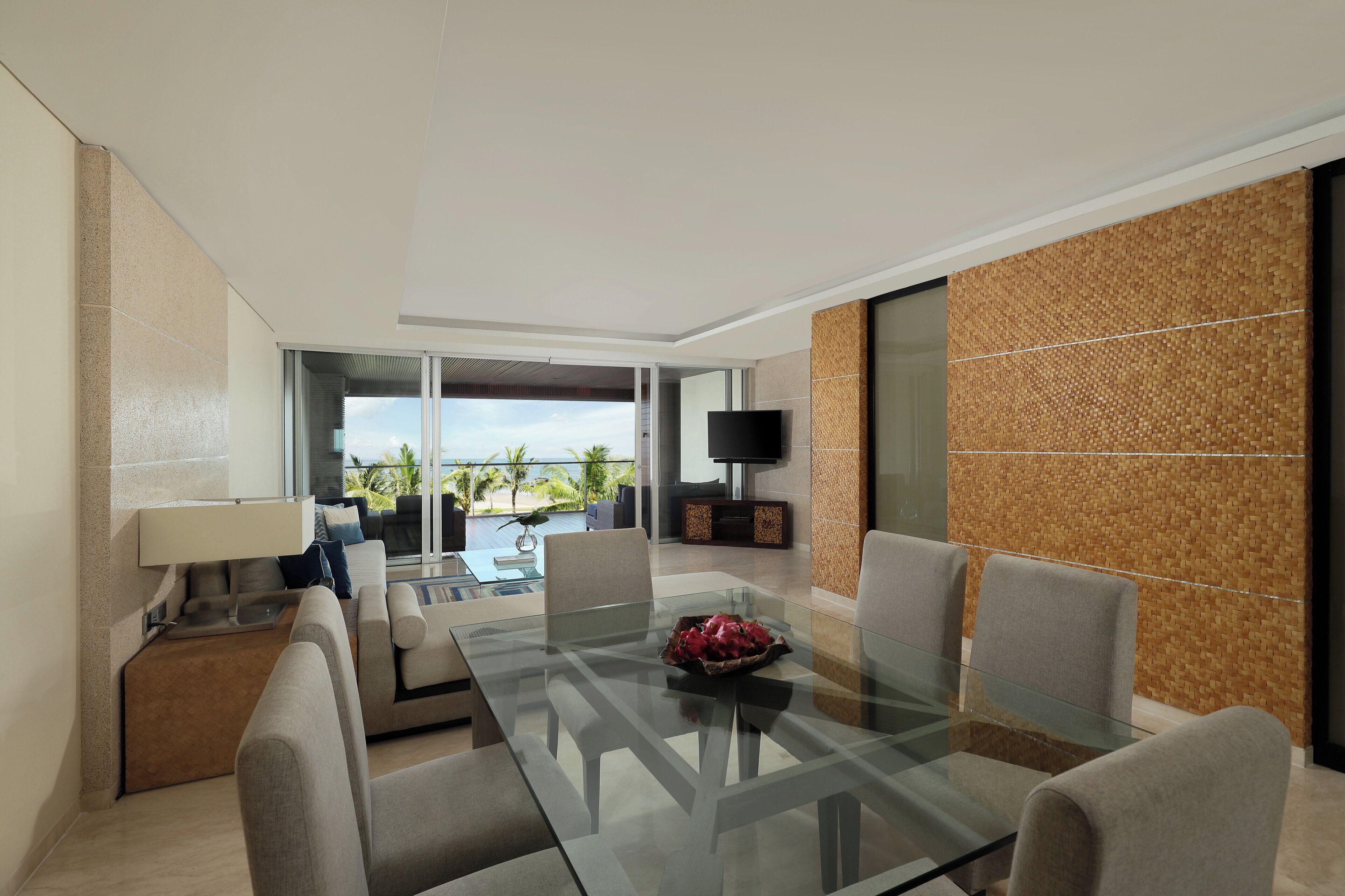 A modern living room with a glass dining table, comfortable seating, a flat-screen TV, and a view of the outdoors.
