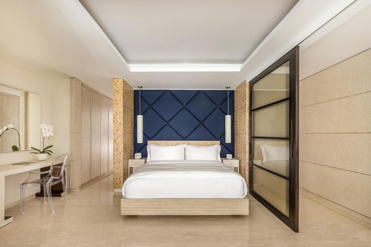 A modern hotel room with a large bed, a desk, and a mirror.