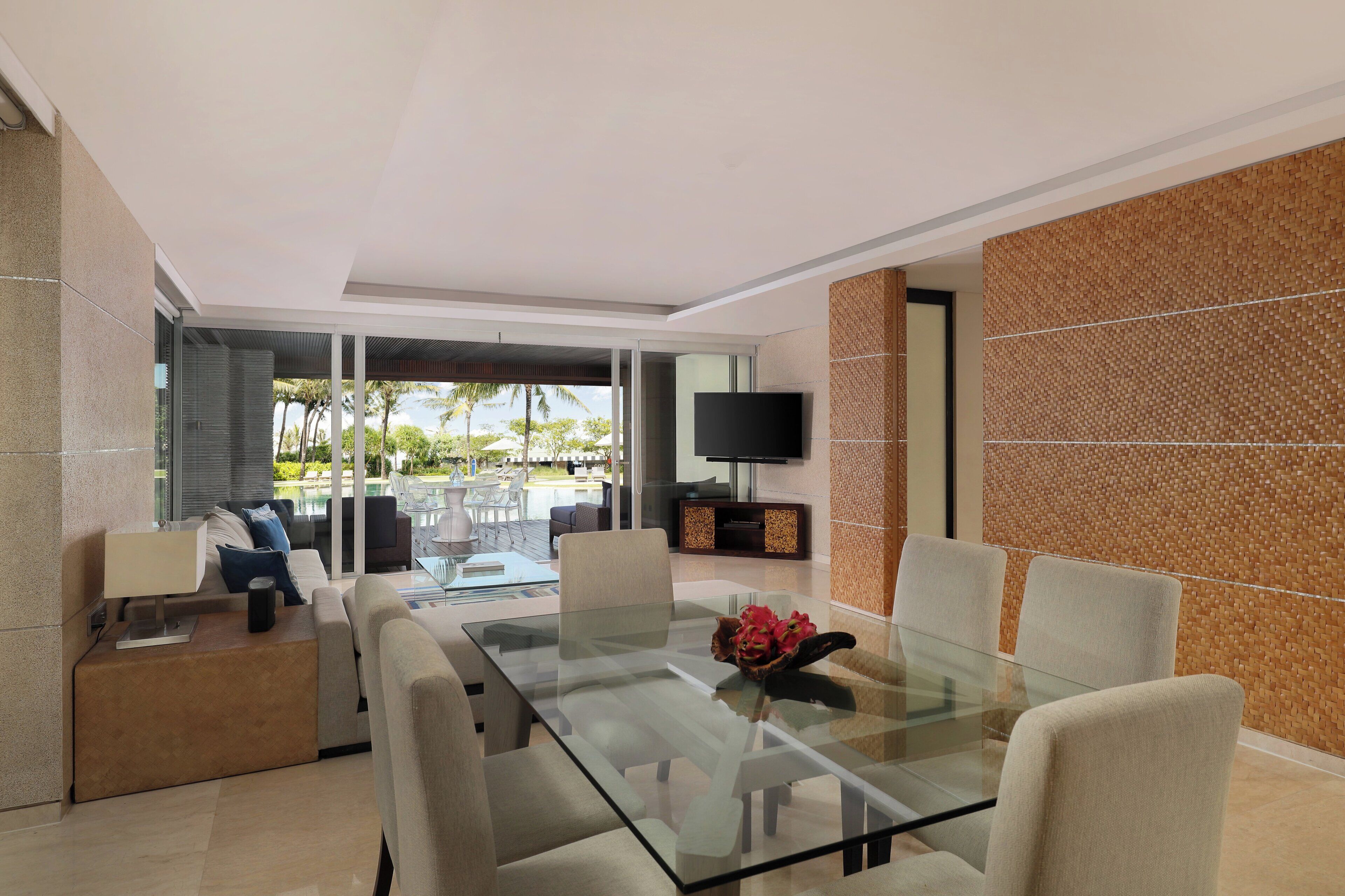 A modern living room with a glass dining table, comfortable seating, a flat-screen TV, and a view of the outdoors.