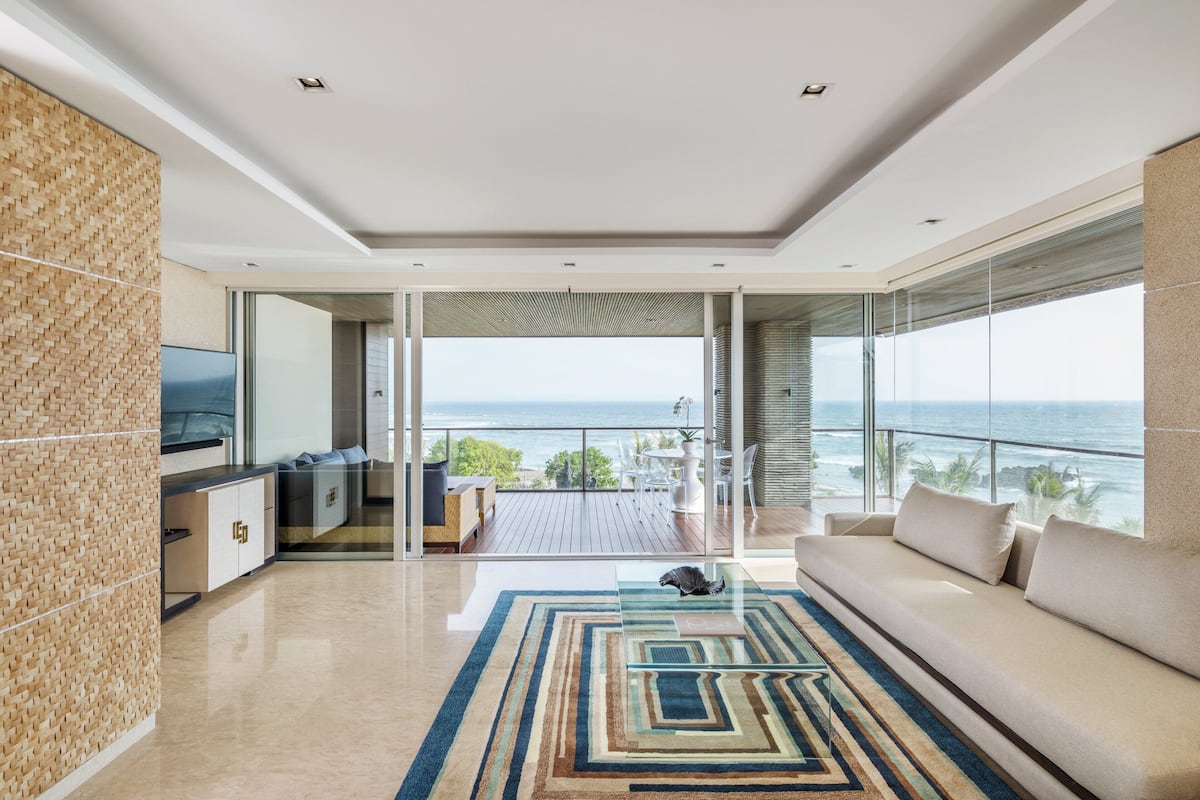 A modern living room with a large sofa, a TV, and a view of the ocean.