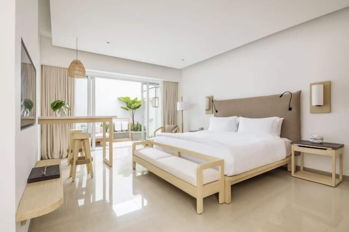 Una habitación de hotel moderna con cama, mesita de noche, lámpara y un escritorio con silla.