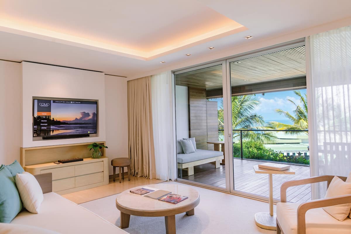 A modern living room with a TV, sofa, coffee table, and a balcony with a view of palm trees.