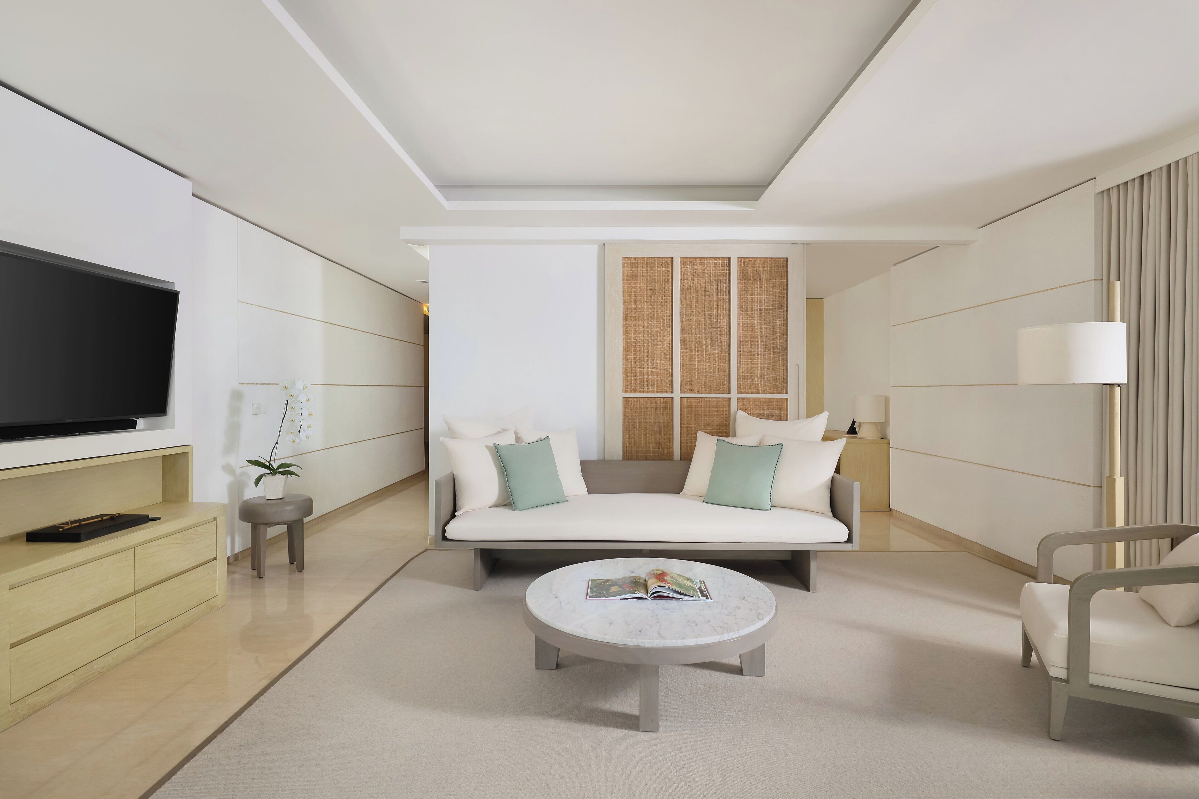 A modern hotel room with a sofa, a coffee table, a TV, and a lamp.