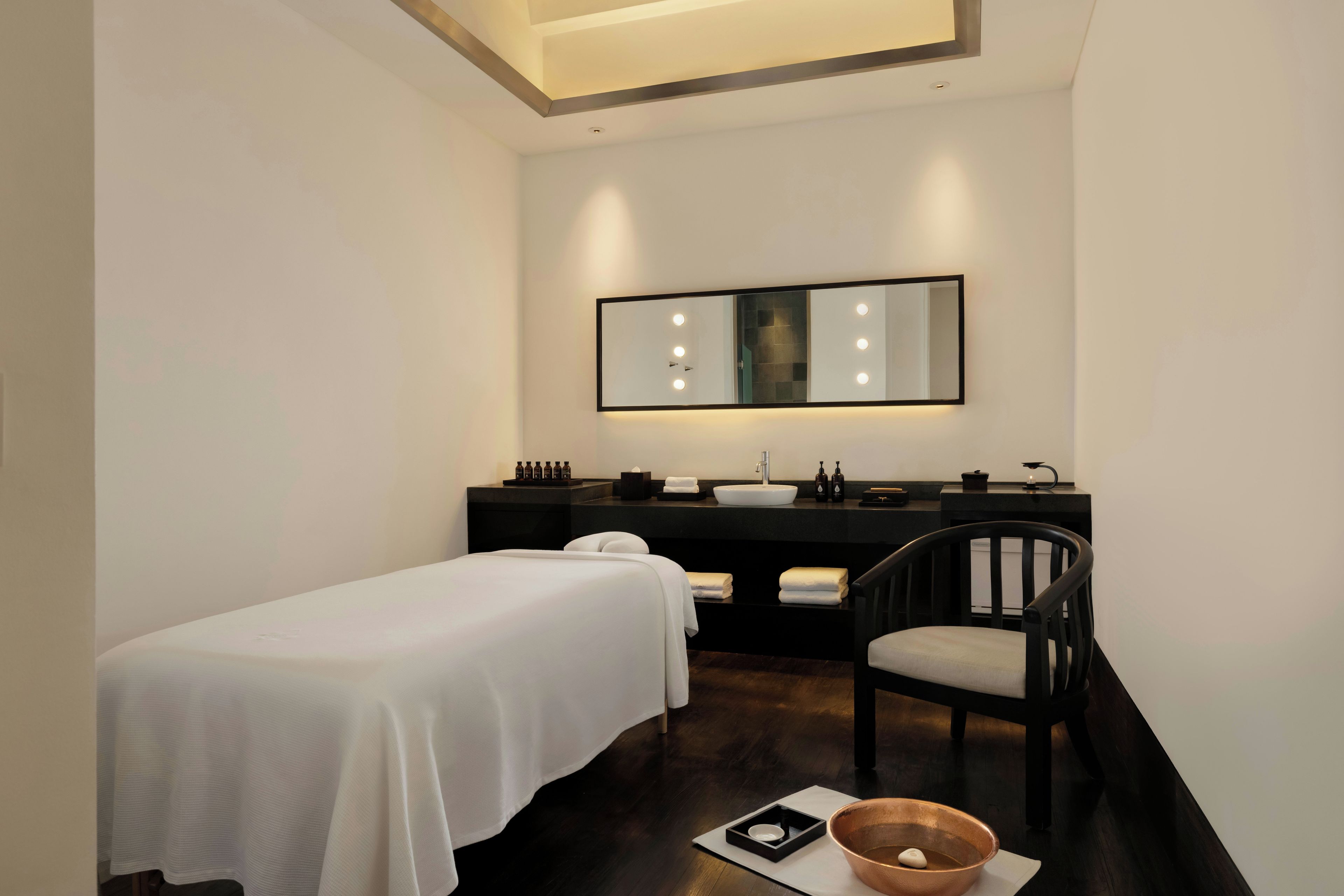 Ein Hotelzimmer mit einem Einzelbett, einem Sessel, einem Schminktisch mit Spiegel und einem kleinen Tisch mit einer Schüssel.