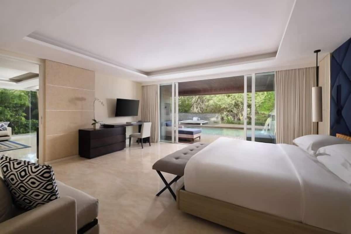 Habitación de hotel moderna con una cama grande, un escritorio, un televisor y vistas a una piscina y follaje.