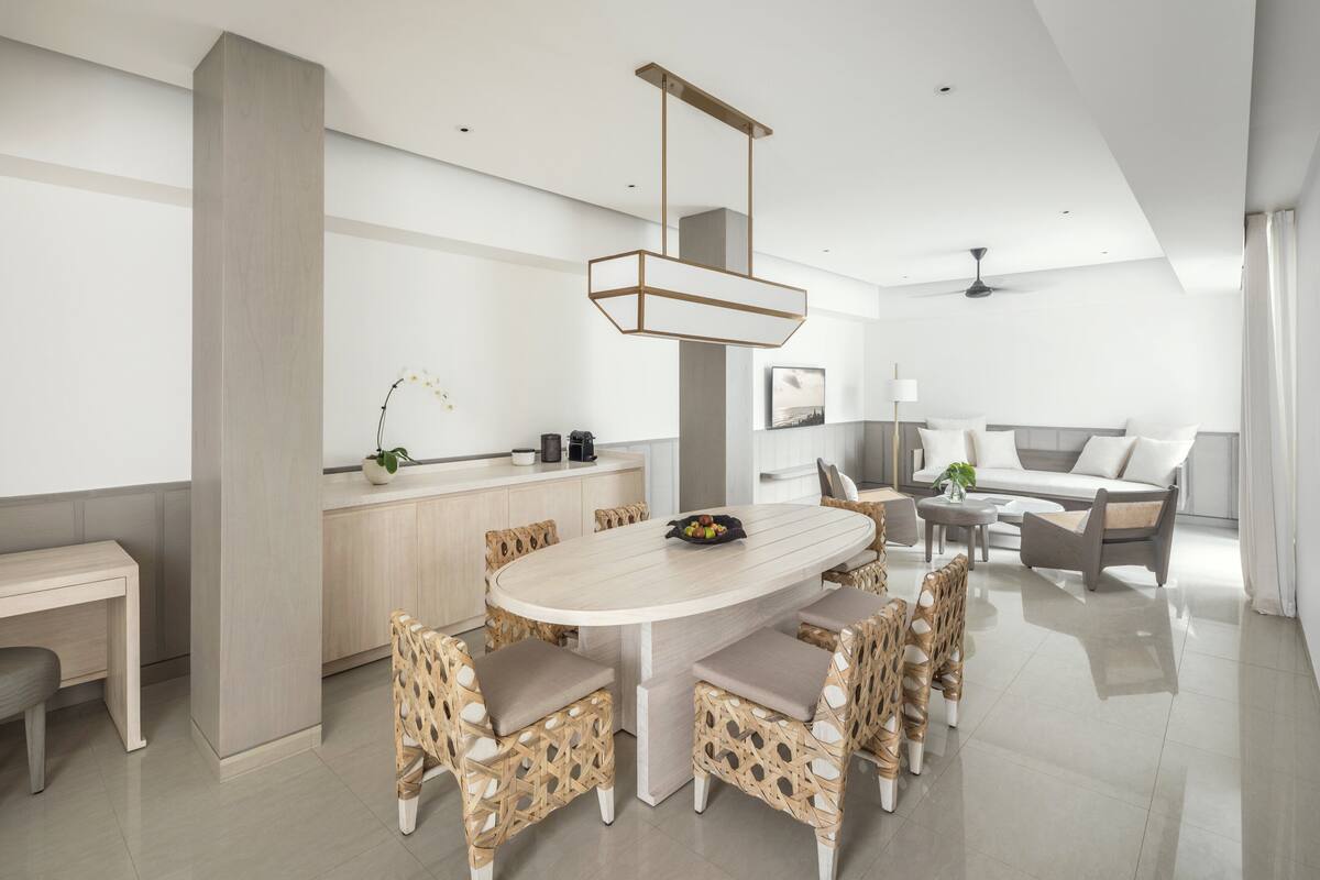 Una sala de estar moderna con una gran mesa ovalada para comer rodeada de sillas de mimbre, un sofá y una mesa de centro.