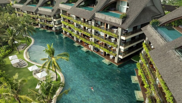 A multi-story hotel with a swimming pool, outdoor seating, and lush greenery.