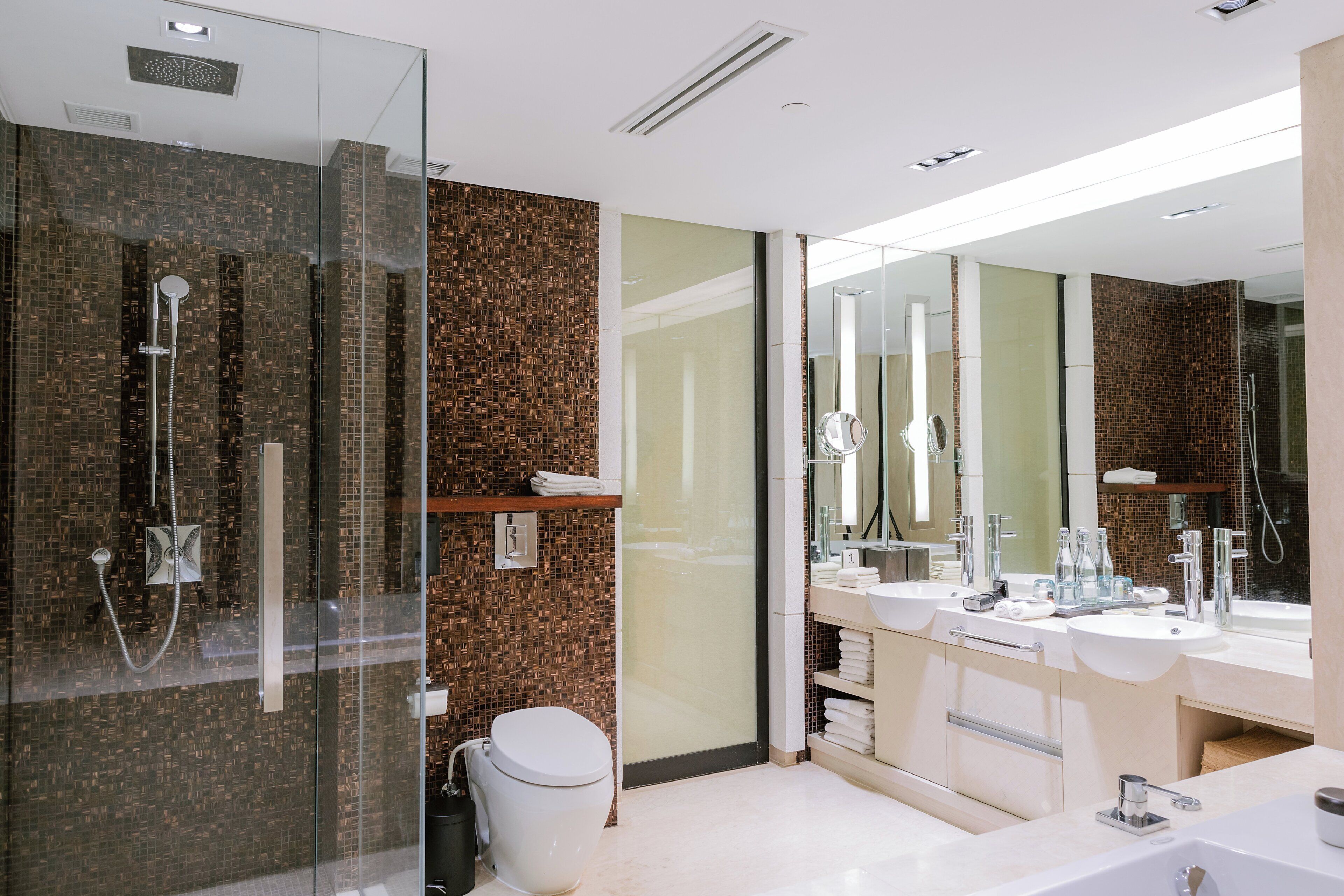 A modern bathroom with a glass-enclosed shower, a white toilet, and a vanity with two sinks.