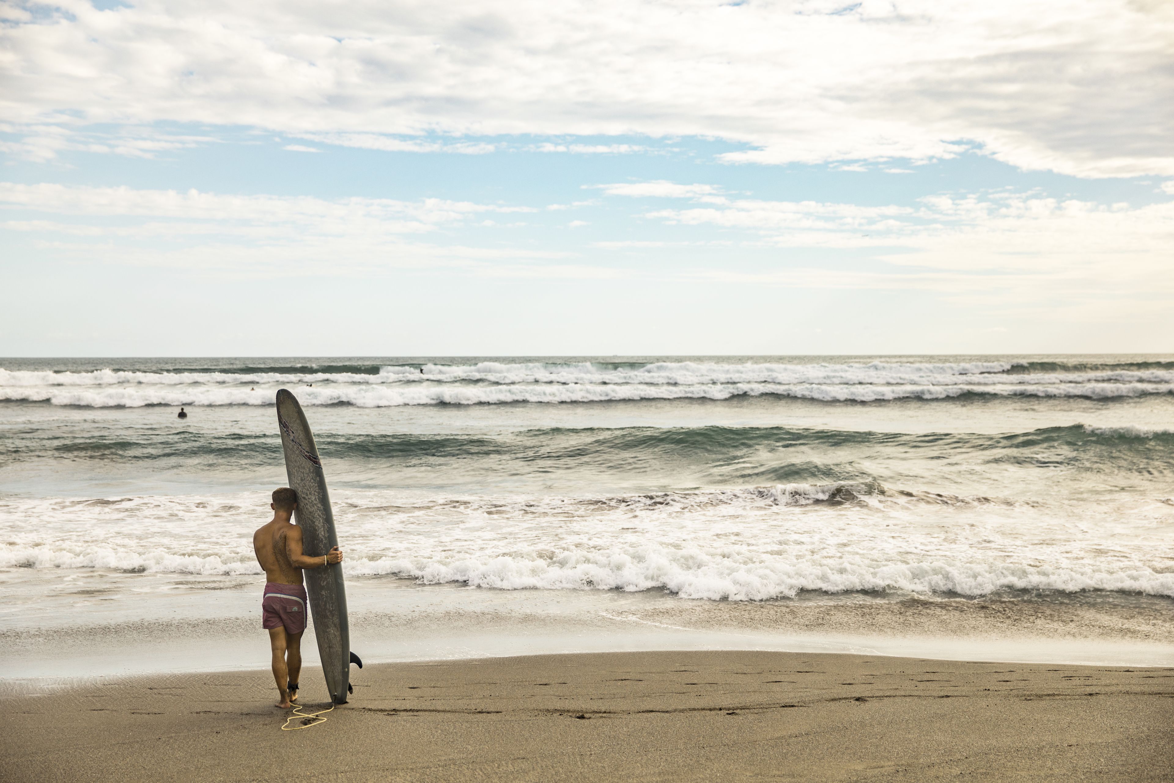 Eine Strandansicht mit einer Person, die ein Surfbrett hält.