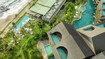 An aerial view of a resort with multiple swimming pools, a beach, and lush greenery.