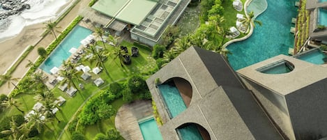 An aerial view of a resort with multiple swimming pools, a beach, and lush greenery.