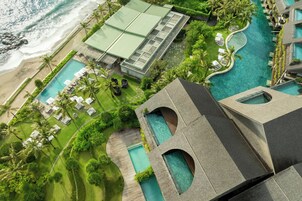 An aerial view of a resort with multiple swimming pools, a beach, and lush greenery.