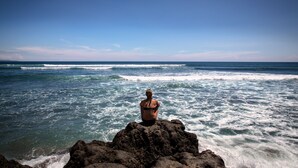 A person sitting on a rocky outcrop overlooking the ocean.