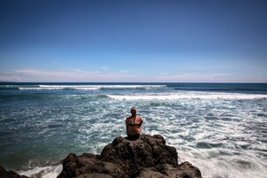 A person sitting on a rocky outcrop overlooking the ocean.
