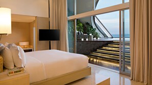 A modern hotel room with a large bed, a flat-screen TV, and a view of a staircase leading to a balcony. - COMO Uma Canggu (Canggu)
