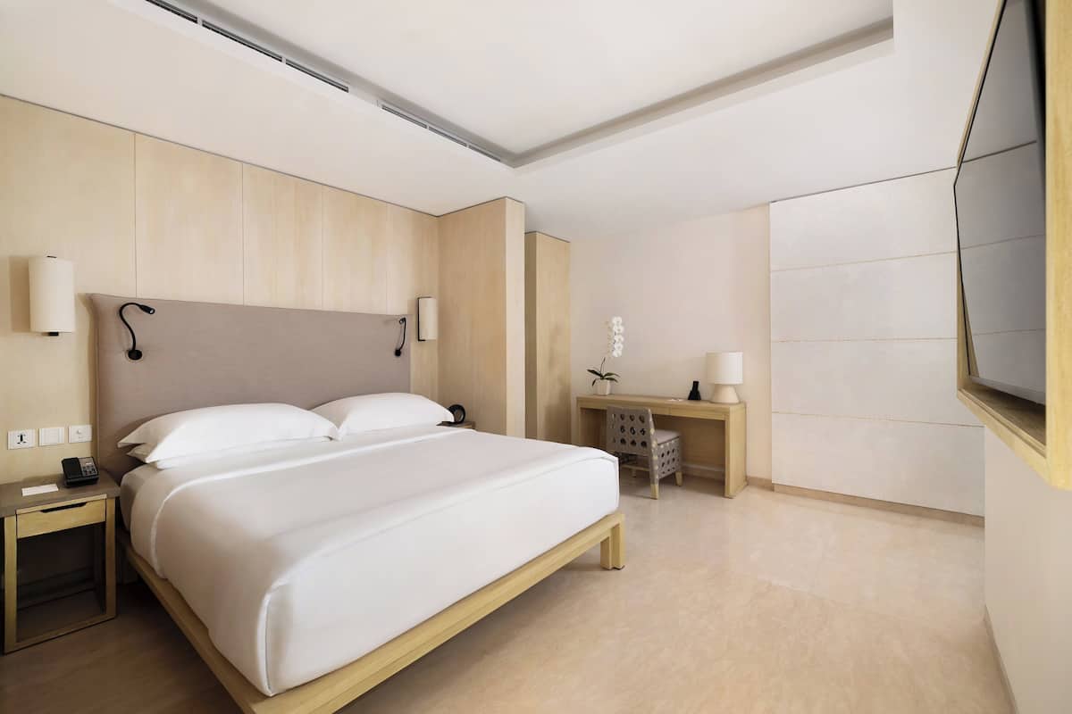 A modern hotel room with a large bed, bedside tables, a desk, and a TV.