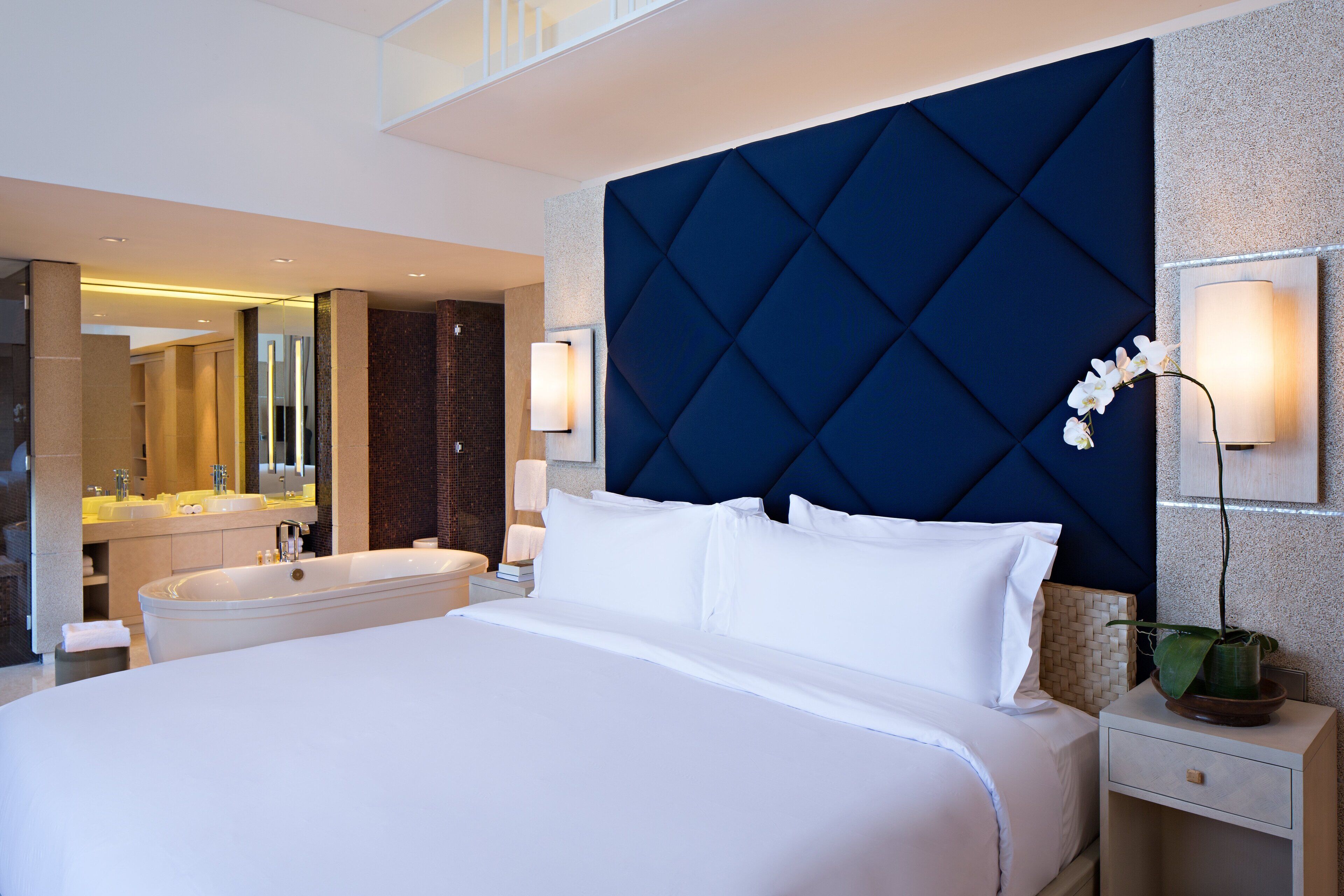 A modern hotel room with a large bed, a bathtub, and a separate bathroom with a mirror and sink.
