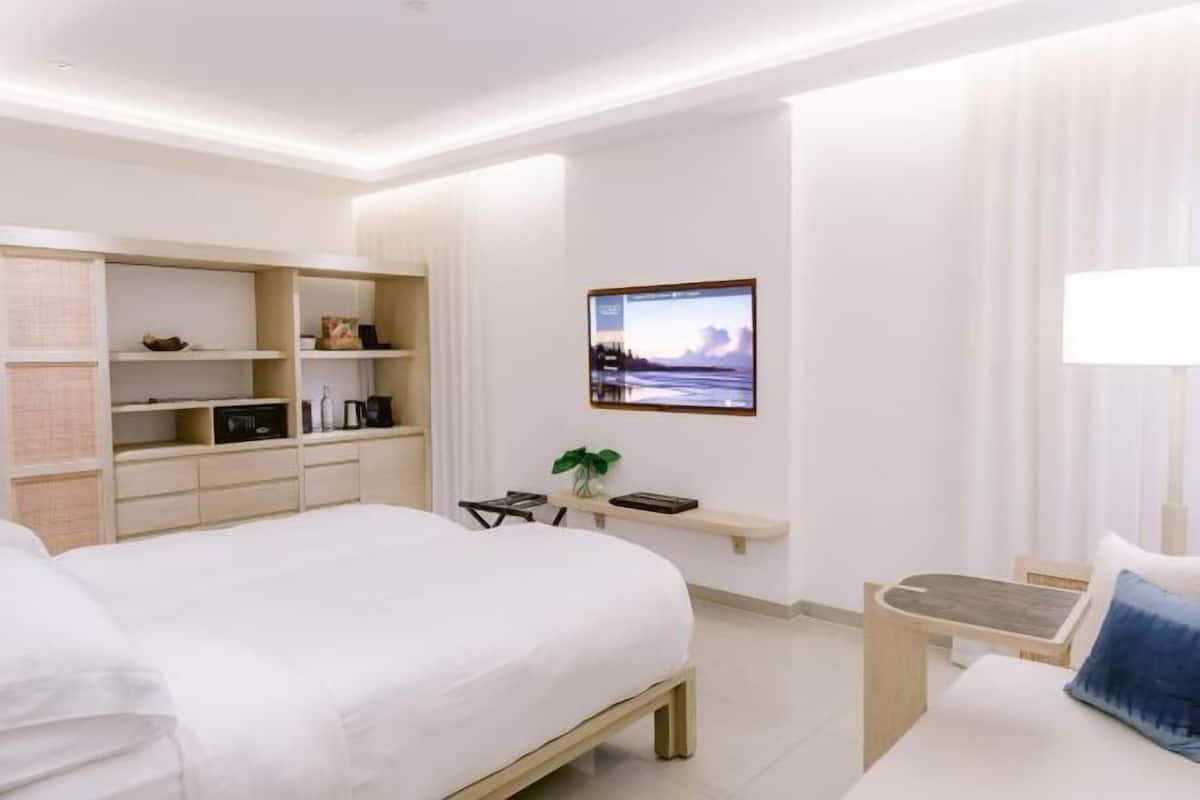 A hotel room with a bed, bedside tables, a desk, shelves, and a wall-mounted TV.