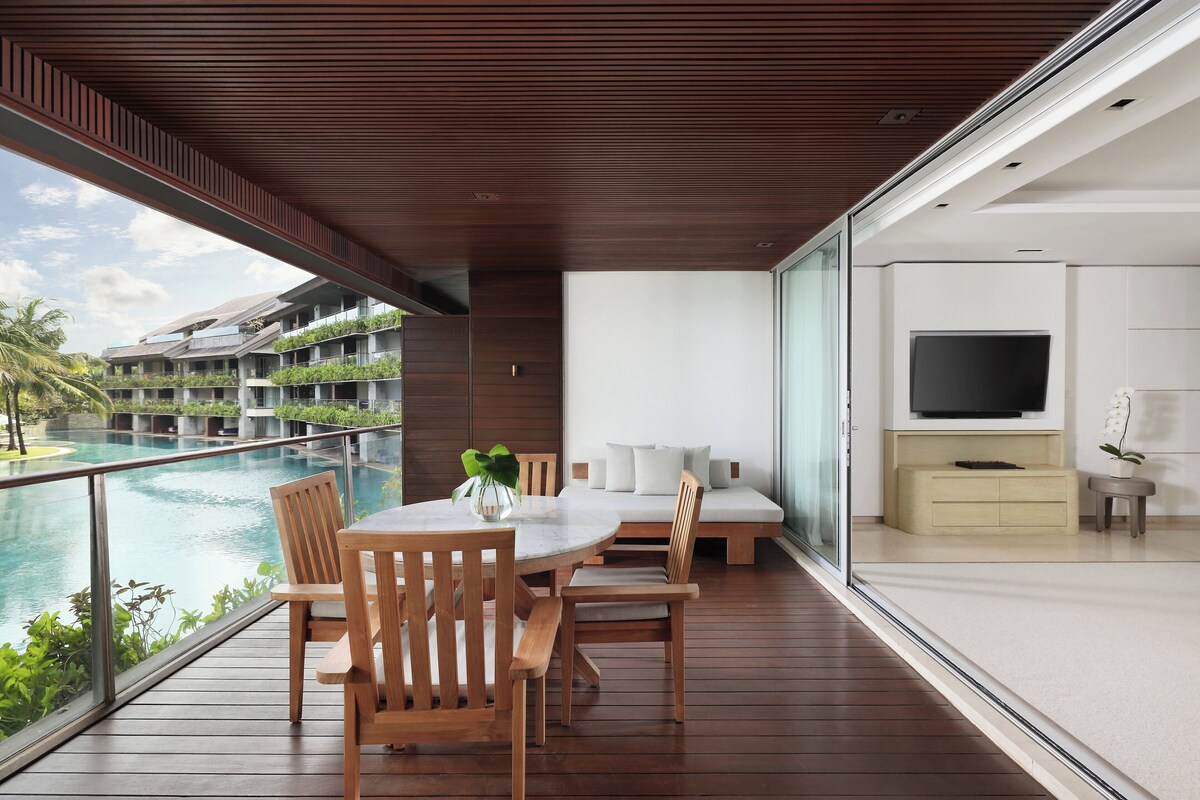A modern balcony with a wooden table and chairs, overlooking a swimming pool and lush greenery.