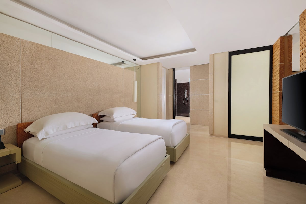 A modern hotel room with two beds, a flat-screen TV, and a large mirror.