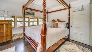 A four-poster canopy bed with a wooden finish, a dresser with multiple drawers, a door with a coat rack, and a window with a view of trees. - Kerrville Area Home w/ Outdoor Entertainment Space (Mountain Home)