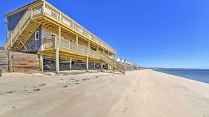 Ein Gebäude direkt am Strand mit mehreren Terrassen und einer Holztreppe zum Strand.