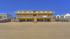 Ein Gebäude direkt am Strand mit einer Holzterrasse und mehreren Balkonen, das auf Stelzen steht.