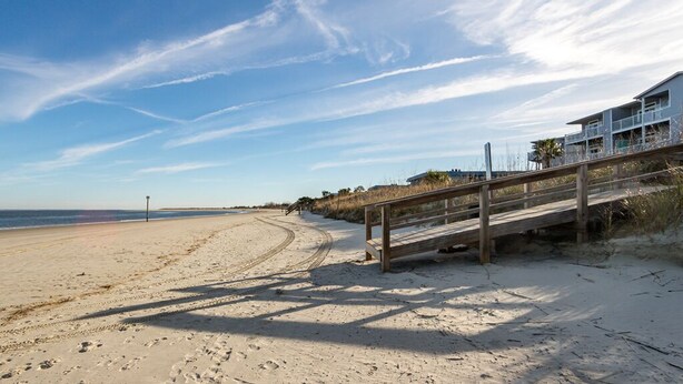 A beach with a wooden walkway leading to a building with balconies overlooking the ocean. - Blue Skies | Game Room, Fire Pit & More! (Tybee Island)
